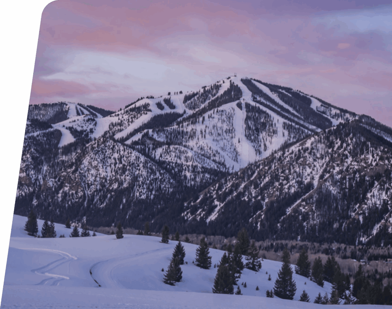 Snowy mountain landscape with pinkish sunset sky.